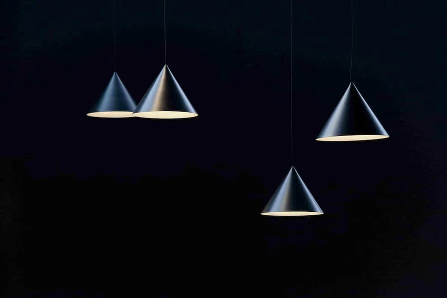 Three modern cone-shaped pendant lights with metallic silver-gray bodies and a warm yellow light glowing from the interior, suspended against a very dark black background.